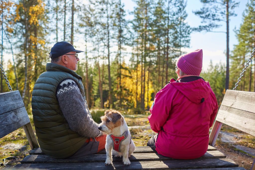 Kaksi retkeilijää istuvat koiran kanssa, taustalla ruskamaisema